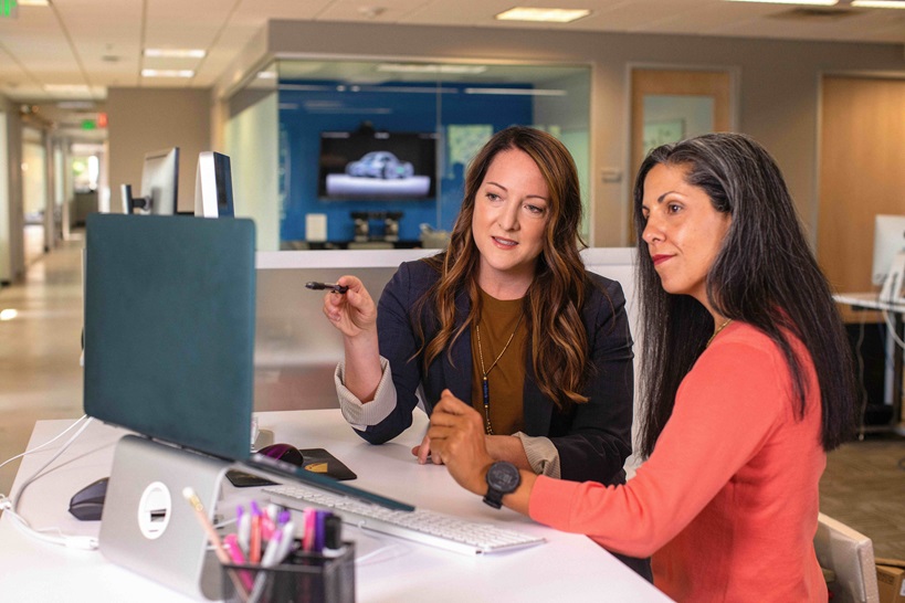 An office environment showing two ladies collaborating on the same side of a desk